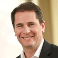 A man with short dark hair, wearing a black suit jacket and white shirt, smiling in a softly lit indoor setting, reflects confidence—ideal for roles in AI fraud detection or digital fraud prevention.