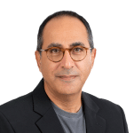 A man with short dark hair and glasses, wearing a dark blazer over a gray shirt, poses against a plain light background—ready to share insights on the evolving cybersecurity landscape in his latest video.