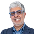 Smiling older man with gray hair, blue glasses, and a blue blazer over a button-up shirt, facing the camera against a white background—ready to represent Cybericon2024.