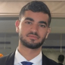 A man with short dark hair and a trimmed beard is wearing a suit and tie, looking at the camera with a neutral expression, ready to attend Cybericon2024.