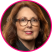 Woman with long brown hair and glasses, wearing a black top, pictured in a headshot with a blurred background and a pink circular border—an advocate for fraud prevention and strong security tactics.