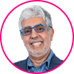 Smiling man with gray hair and beard wearing blue glasses and a blazer, pictured in front of a white background with a pink circular border, representing a collaborative approach essential in the digital era.
