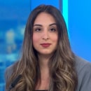 A woman with long brown hair and a gray blazer sits in a studio setting with blue lighting in the background, ready to discuss the highlights of CyberWeek 2024.